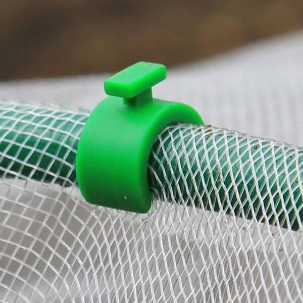 A close-up of a green hoop clip securing a mesh to a flexible garden hoop.