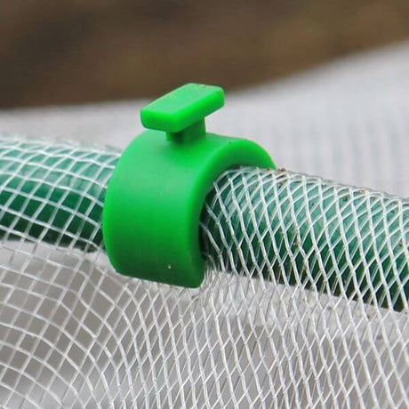 A close-up of a green hoop clip securing a mesh to a flexible garden hoop.