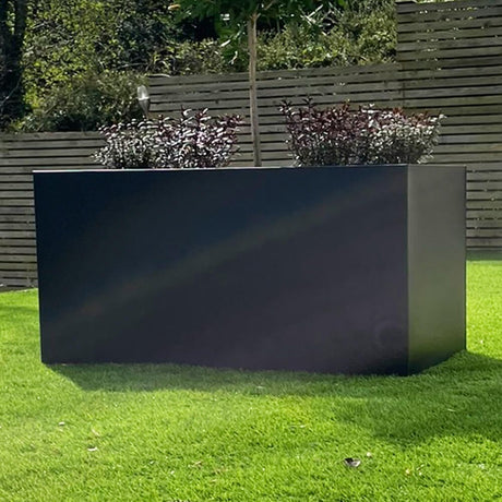 A large rectangular black zinc trough patio planter placed on a grassy area with a wooden fence in the background. The planter is empty and has a reflective surface.
