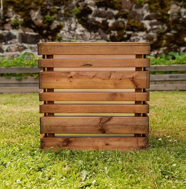 Wooden planter box on grass with a stone wall background