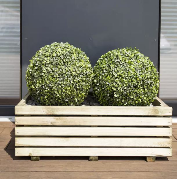 Two spherical green plants in a wooden planter box on a wooden deck.