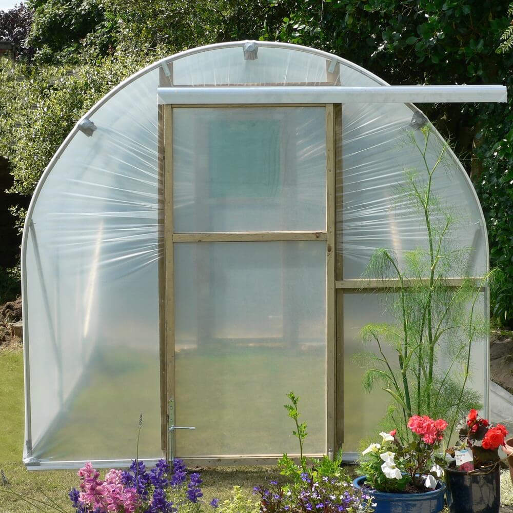 Small greenhouse with plants and flowers in a garden setting