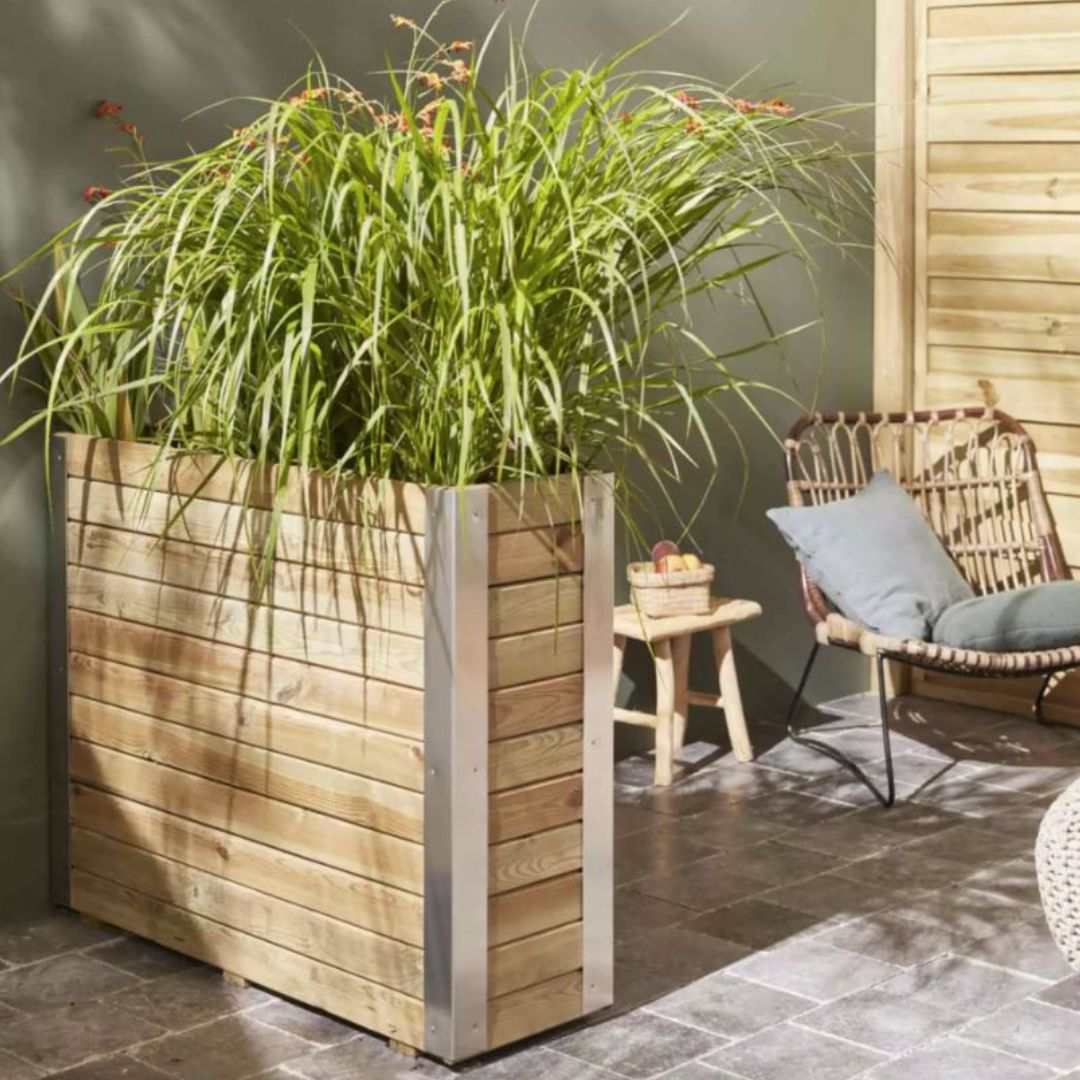 Wooden planter with green plants in an outdoor setting with a chair and table.
