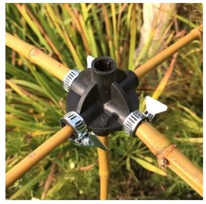 A bamboo cane connector attached to a bamboo structure with metal clamps in a garden setting.