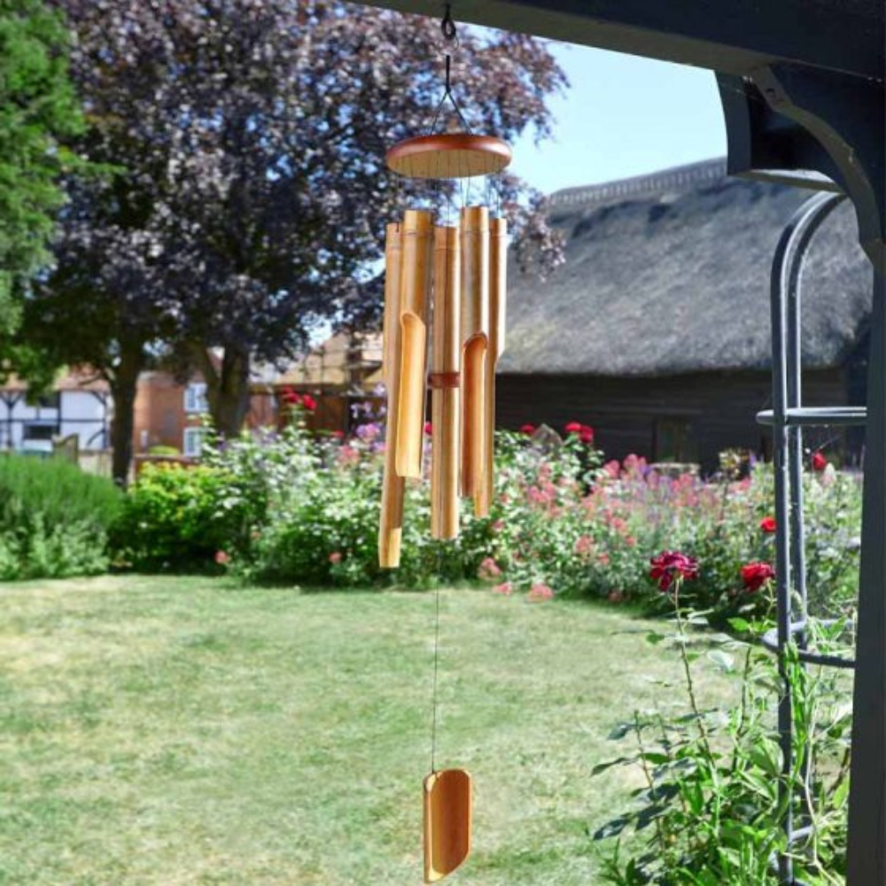 A bamboo wind chime hanging in a garden with a blurred background of flowers and trees.
