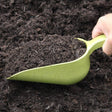 An olive green bamboo compost scoop filled with soil, held by a hand above a pile of soil.