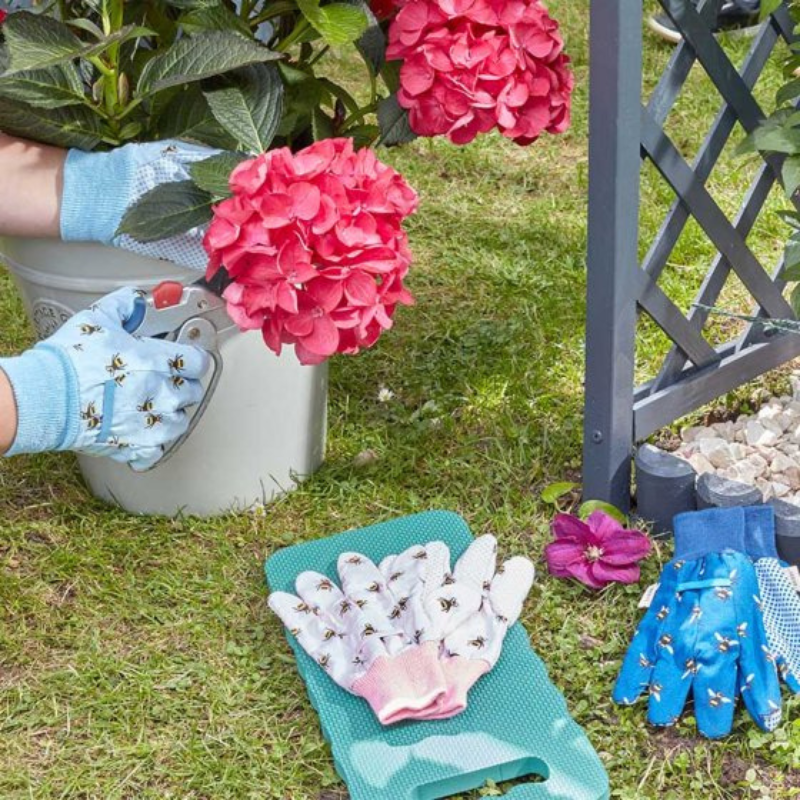 A person gardening wearing blue and pink gardening gloves with a bee design, surrounded by garden tools and plants.