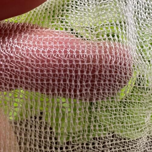 A close-up of biodegradable garden netting made from cornstarch, held in a person's fingers, with foliage in the background.