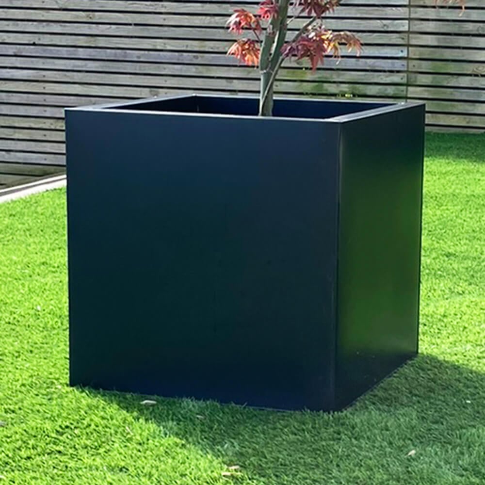 Black cube plant pot in garden with fence in background