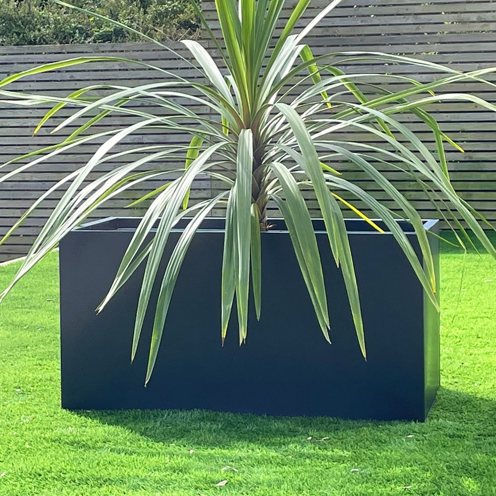 Black Aluizinc trough planter with tropical plant, wooden fence on grass