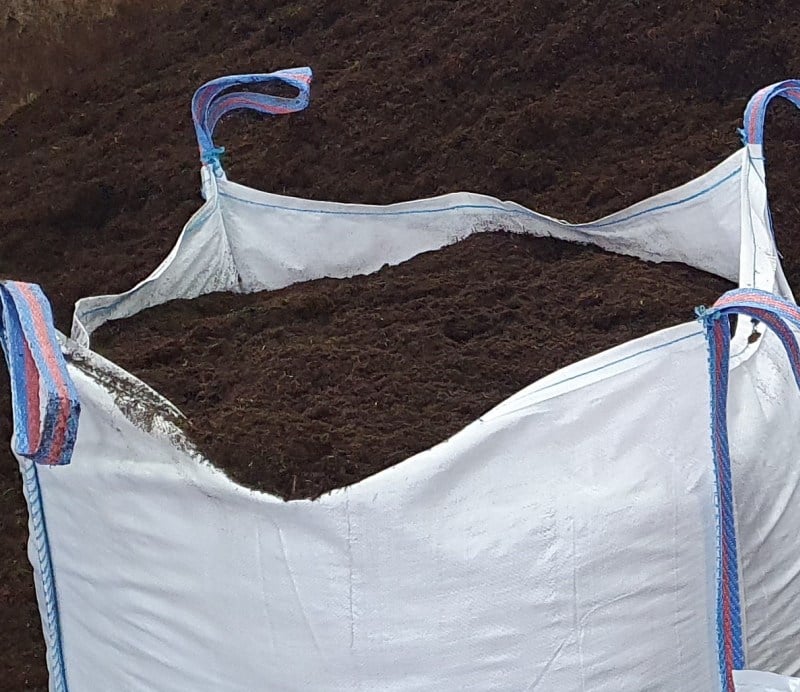 A bulk bag of brown wool compost, with the bag partially opened, showing the soil inside.