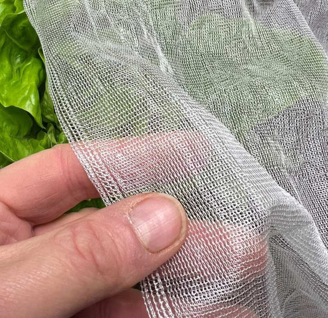 A close-up of biodegradable garden netting made from cornstarch, held in a person's fingers, with foliage in the background.