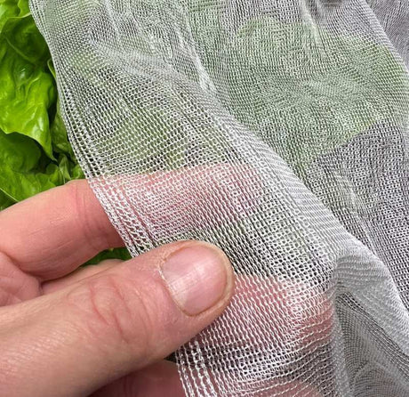A close-up of biodegradable garden netting made from cornstarch, held in a person's fingers, with foliage in the background.