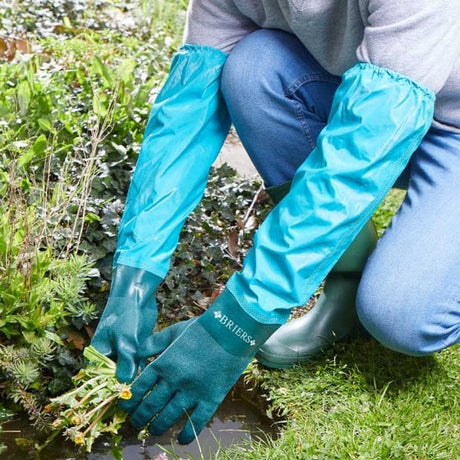 A person wearing long blue waterproof gloves is crouching next to a pond, engaged in garden maintenance.