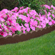 A brown scallop curve border edging installed around a bed of pink flowers on a grassy area.