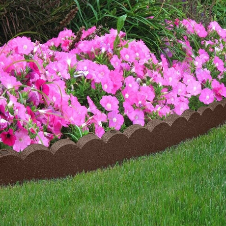 A brown scallop curve border edging installed around a bed of pink flowers on a grassy area.