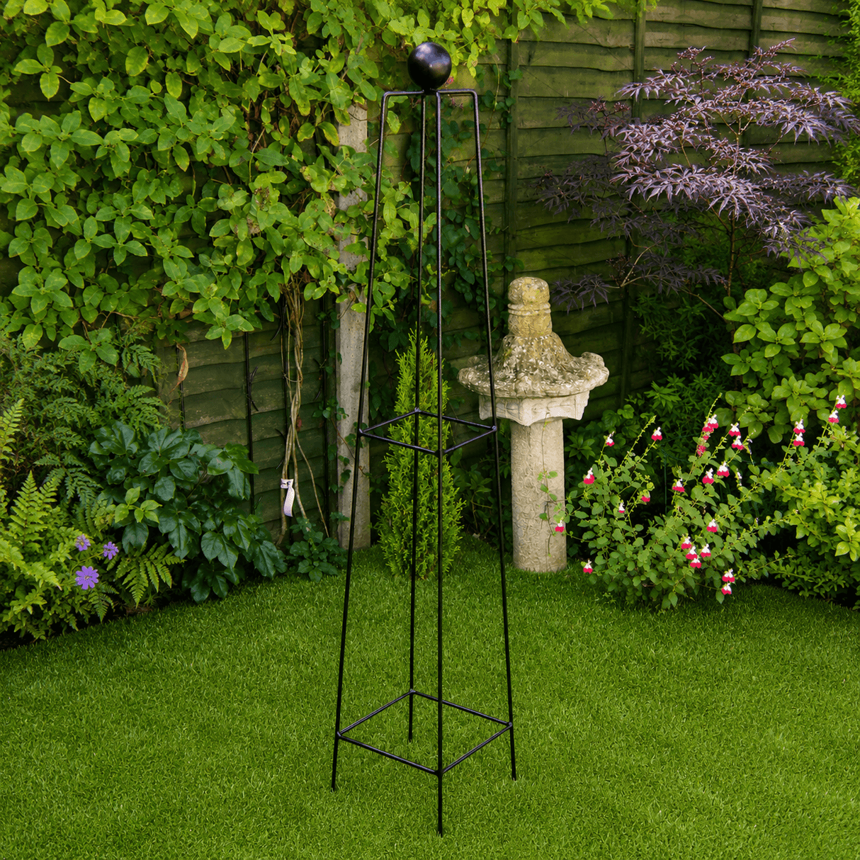 Black metal garden obelisk with decorative top in a garden setting