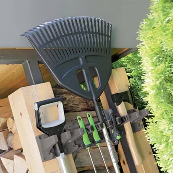 A garden tool holder mounted on a wooden structure, holding various gardening tools such as a rake and a spade.