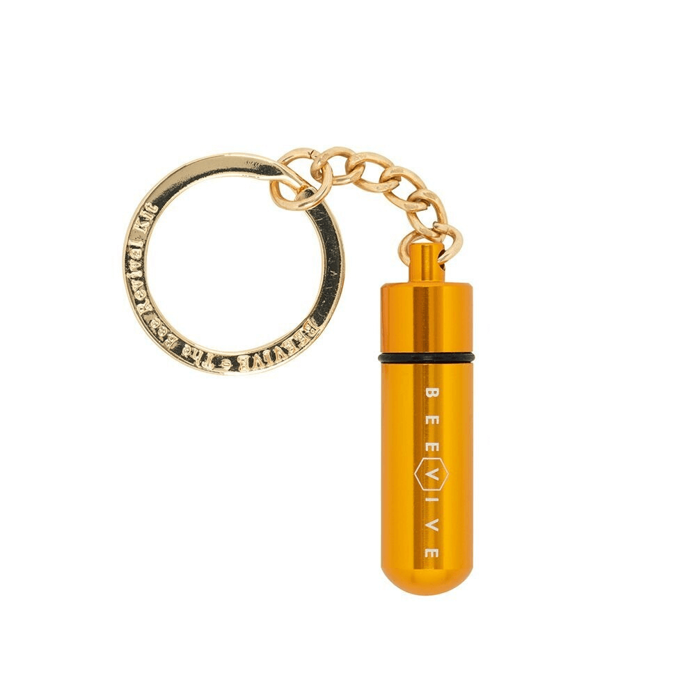 A bee revival kit keychain with a gold-colored tube and a hexagonal pattern in the background.