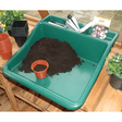 Green potting tray on wooden table with soil and pots