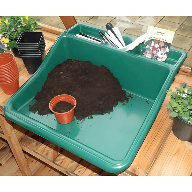 Green potting tray on wooden table with soil and pots