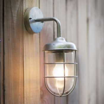 A wall-mounted garden light with a galvanised steel cage and a lit bulb, attached to a wooden surface.