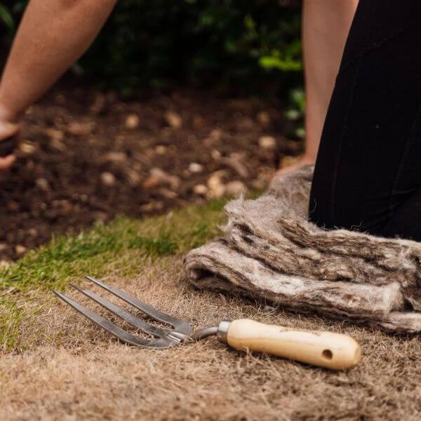 Person showing hortiwool being used on a flower bed as weed ocntrol