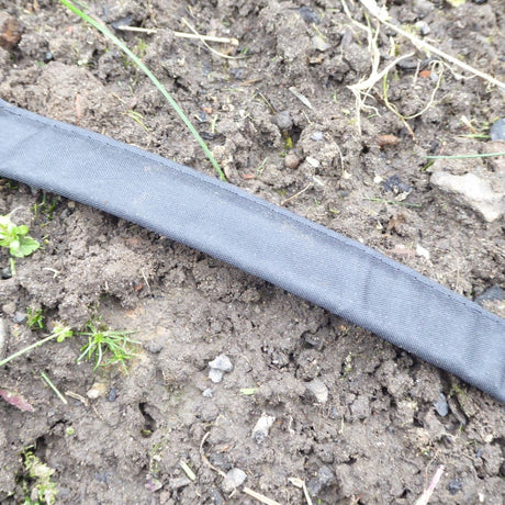 A flat irrigation hose laid on soil with ground securing stakes around it.