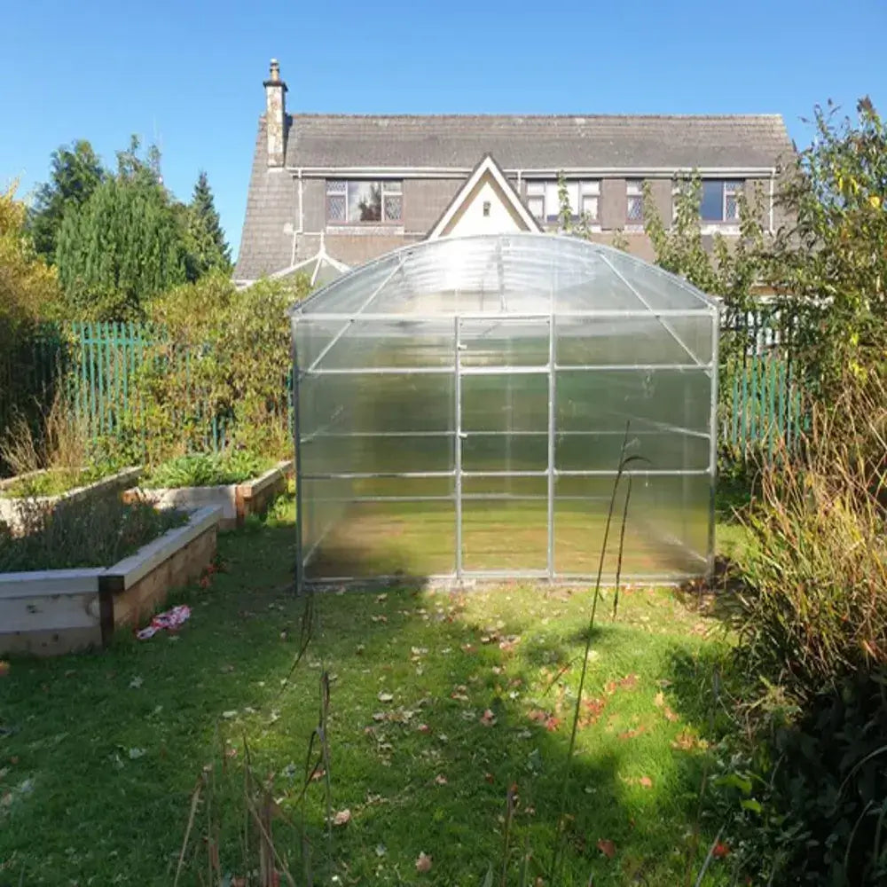 a greenhouse in someone's garden with a house behind