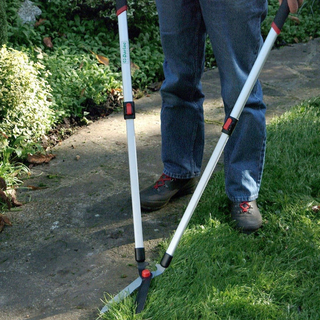A person using telescopic lawn edging shears to trim grass on a garden path.