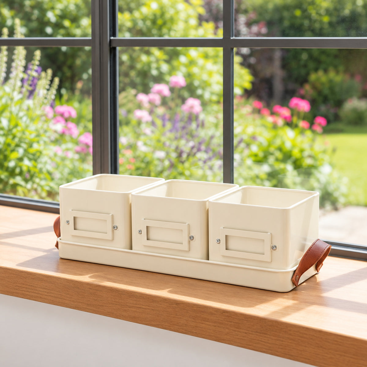 Three cream-colored herb tins, arranged in a row on a wooden windowsill with a blurred garden background.