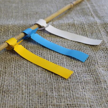 Three colored loop labels (yellow, blue, white) tied on a stick, displayed on a burlap surface