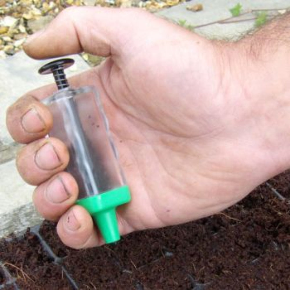 A hand holding a Magic Seeder, a flower seeder for sowing seeds, with a clear body and green accents.