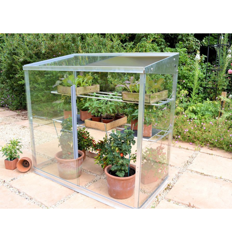 A Midi Growhouse made of aluminum and safety glass, with sliding doors and two shelves inside, placed on a patio.