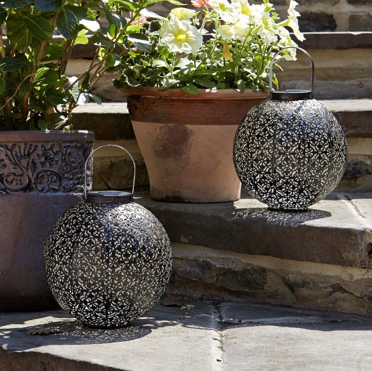 Two moroccan lanterns sat on stone step with plant pots in background