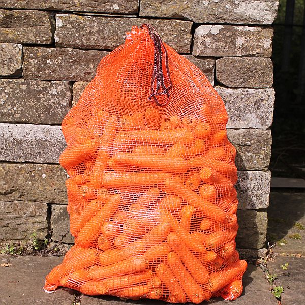 Orange vegetable net full of carrots stood against a stone wall