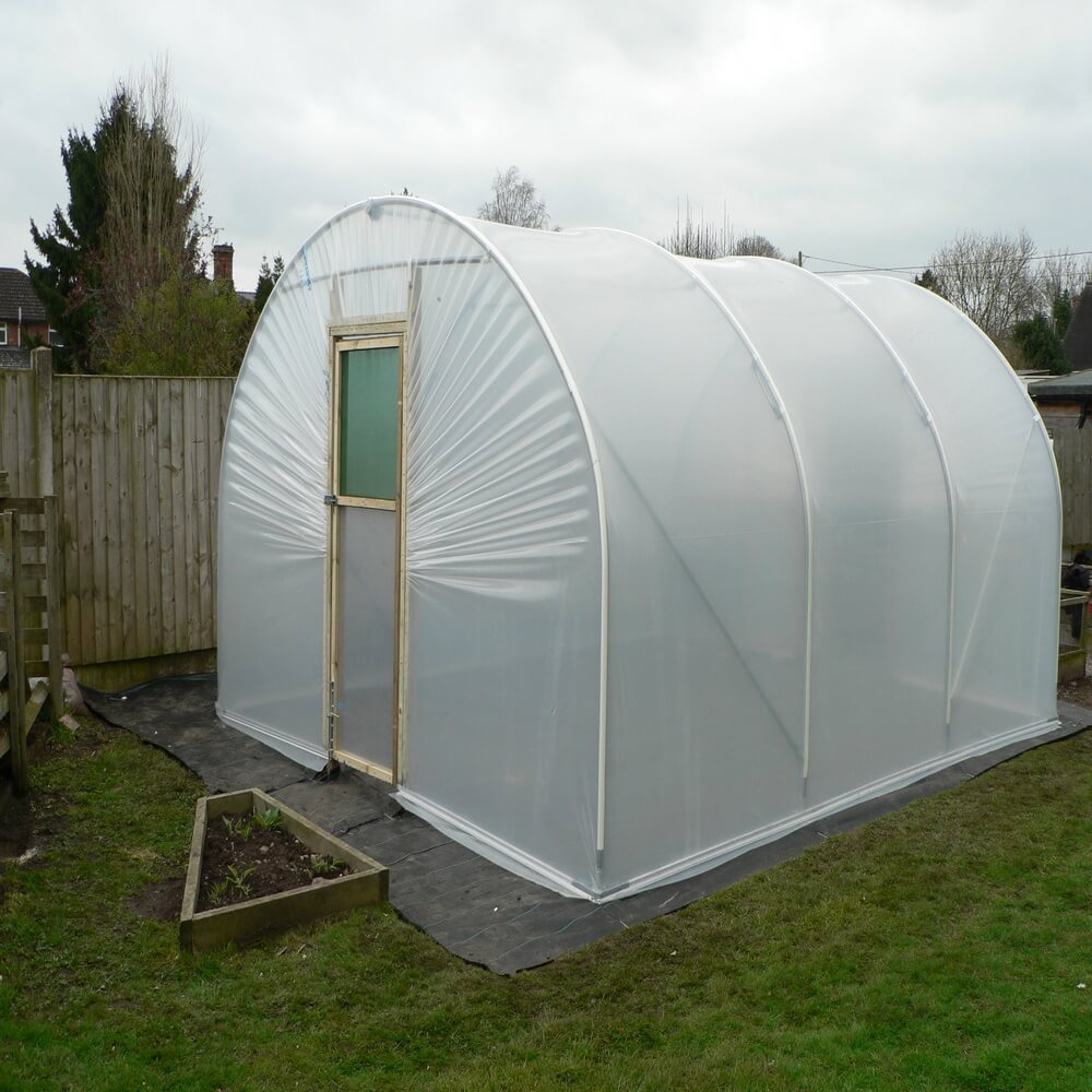 Polycarbonate greenhouse with a wooden door on grass