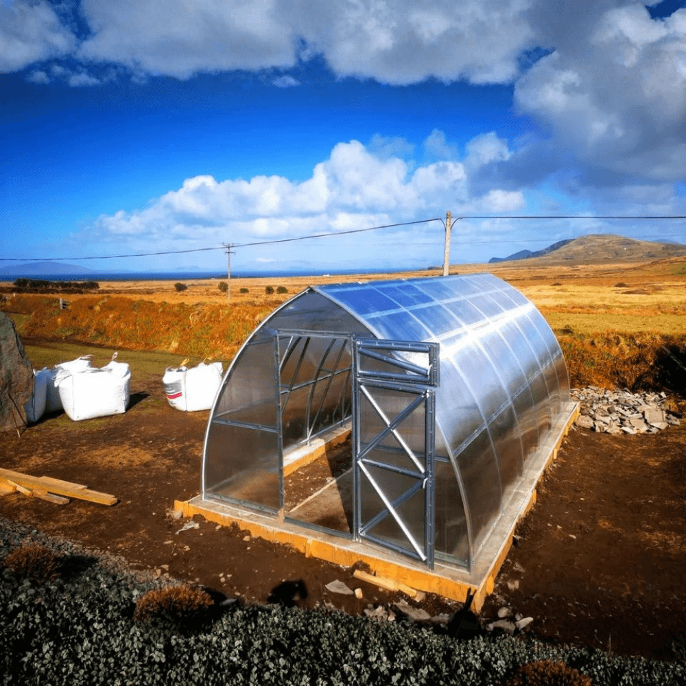 Metal greenhouse in a rural setting with a blue sky and clouds.