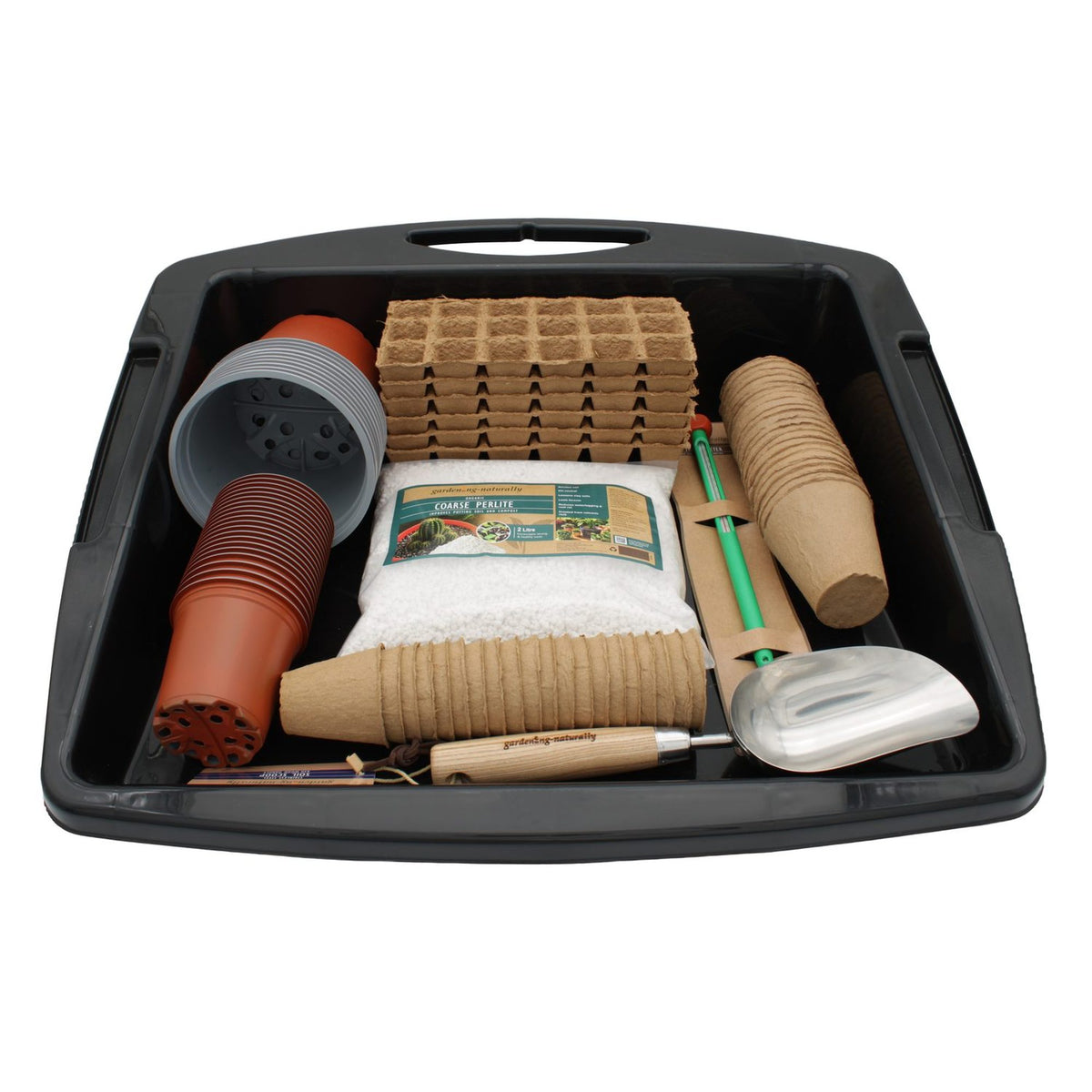 A black plastic seed starter tray filled with gardening tools and starter materials, including seed starts, pots, peat-free coir pots, a hand trowel, and a small hand fork, on a white background.