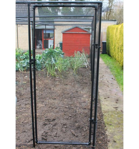A black metal fruit cage door kit installed on a frame with a garden and house in the background.