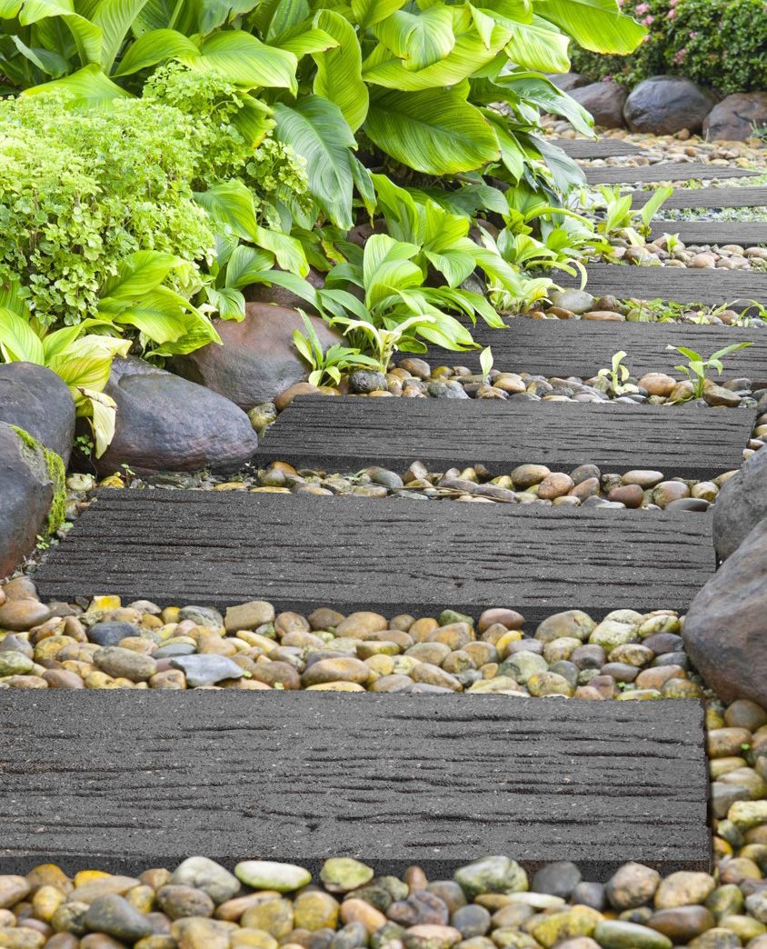 A series of gray railroad tie stepping stones installed on a garden path, surrounded by white pebbles on both sides.