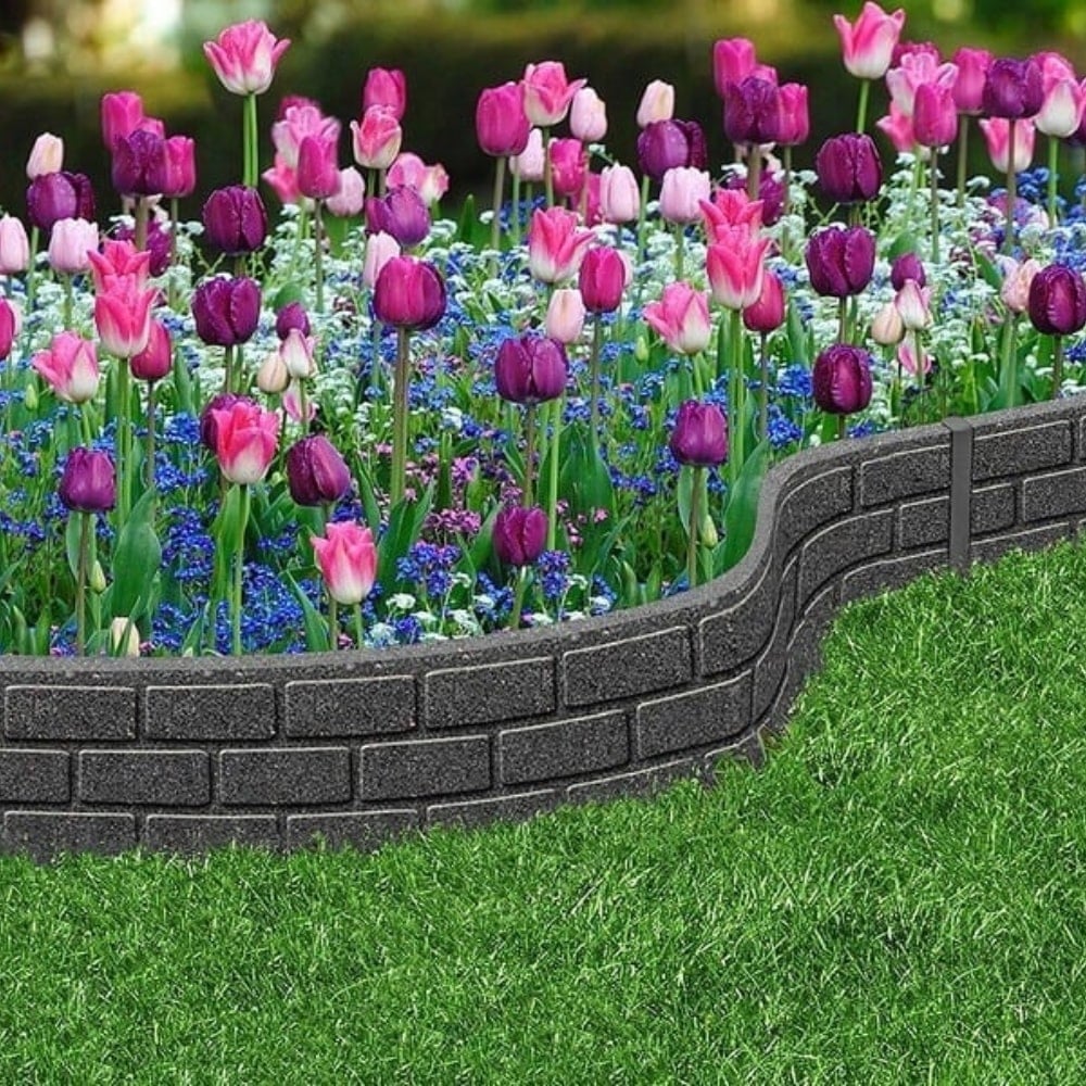 A grey rubber garden border edging brick effect installed around a flower bed with colorful flowers behind it.