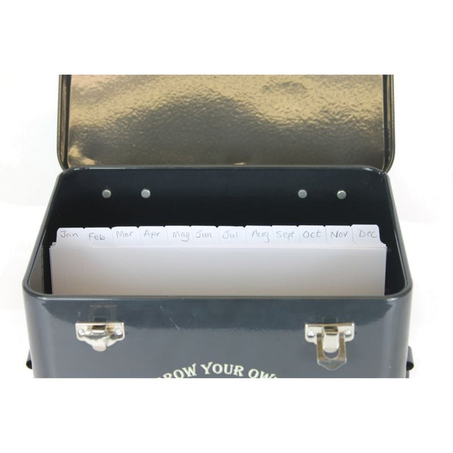A set of white paper dividers with monthly labels, placed inside a black metal seed tin with a lid.