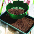 A green seed tray sieve with 3mm mesh being used to sieve soil into a tray.