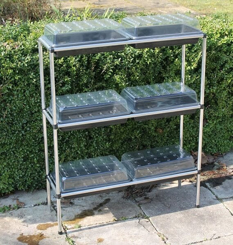 A three-tiered seed tray stand stood in a garden with propagators on
