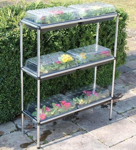 A three-tiered seed tray stand made of aluminum, with each tier holding two seed trays covered with clear plastic lids.