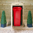 A single wooden wheelie bin storage unit with a red bin visible, placed on a gravel surface, flanked by two artificial green shrub pots.