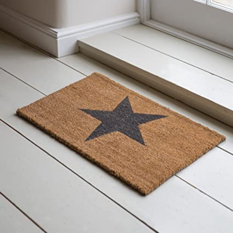 A natural brown coir doormat with a large black star in the center, placed on a white wooden floor.