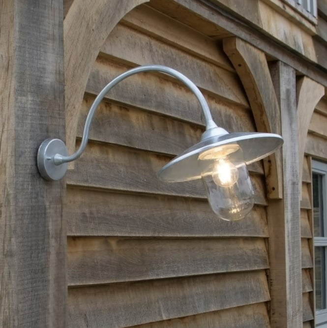 An exterior wall-mounted light fixture with a clear glass shade and a metallic silver finish, mounted on a wooden exterior wall.
