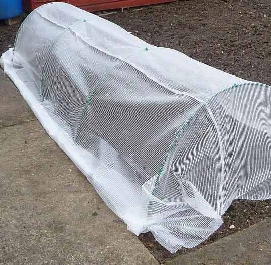 A garden with flexible tunnels covered in white netting, designed to protect plants.